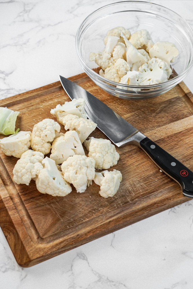 cauliflower chunks on wooden board with knife